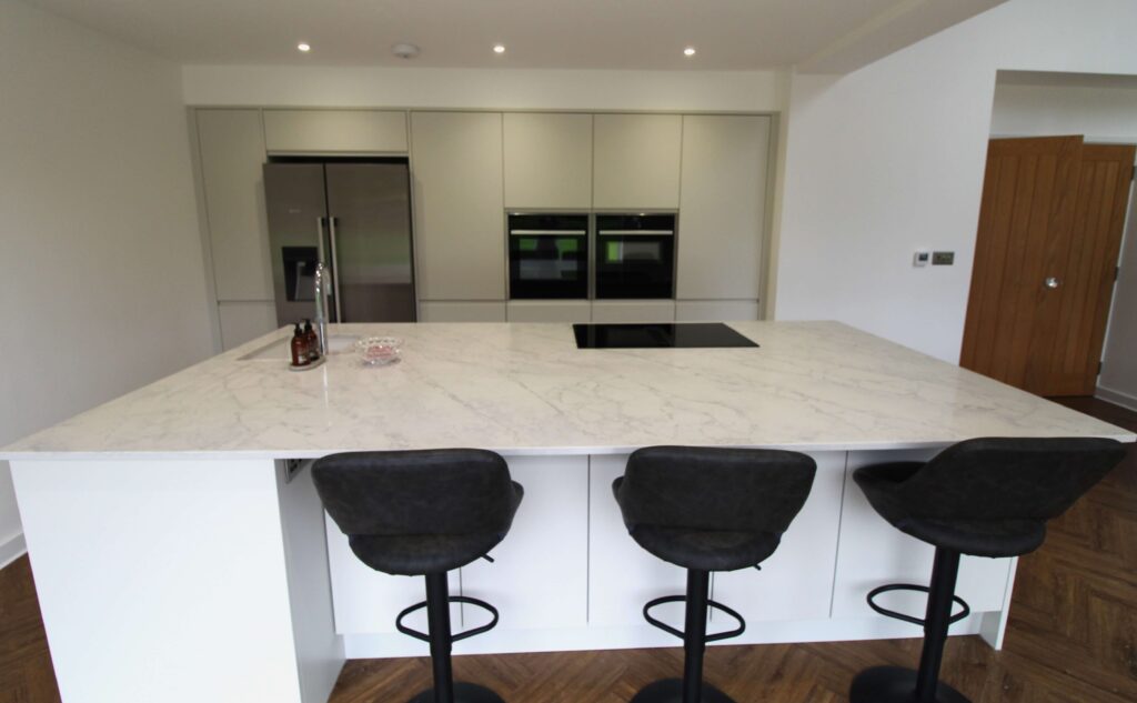 Kitchen island with black stools and quartz worktop with induction hob, sink and quooker tap