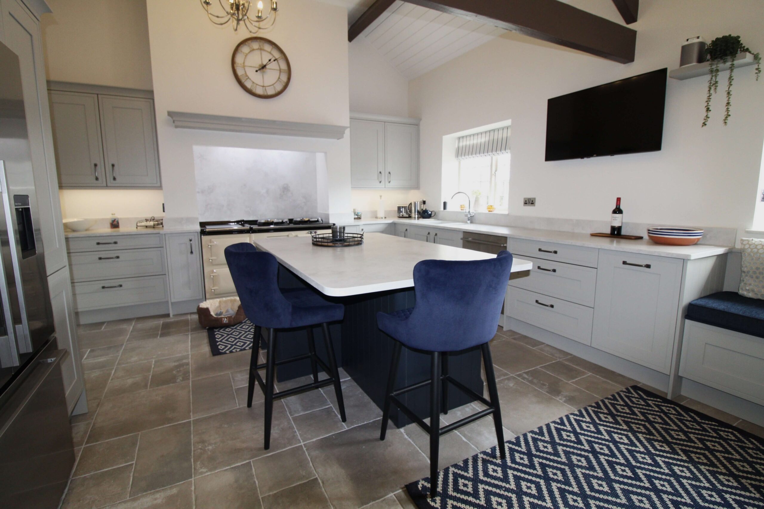 Soft grey painted kitchen with island surrounded by velvet blue stools and a quartz worktop