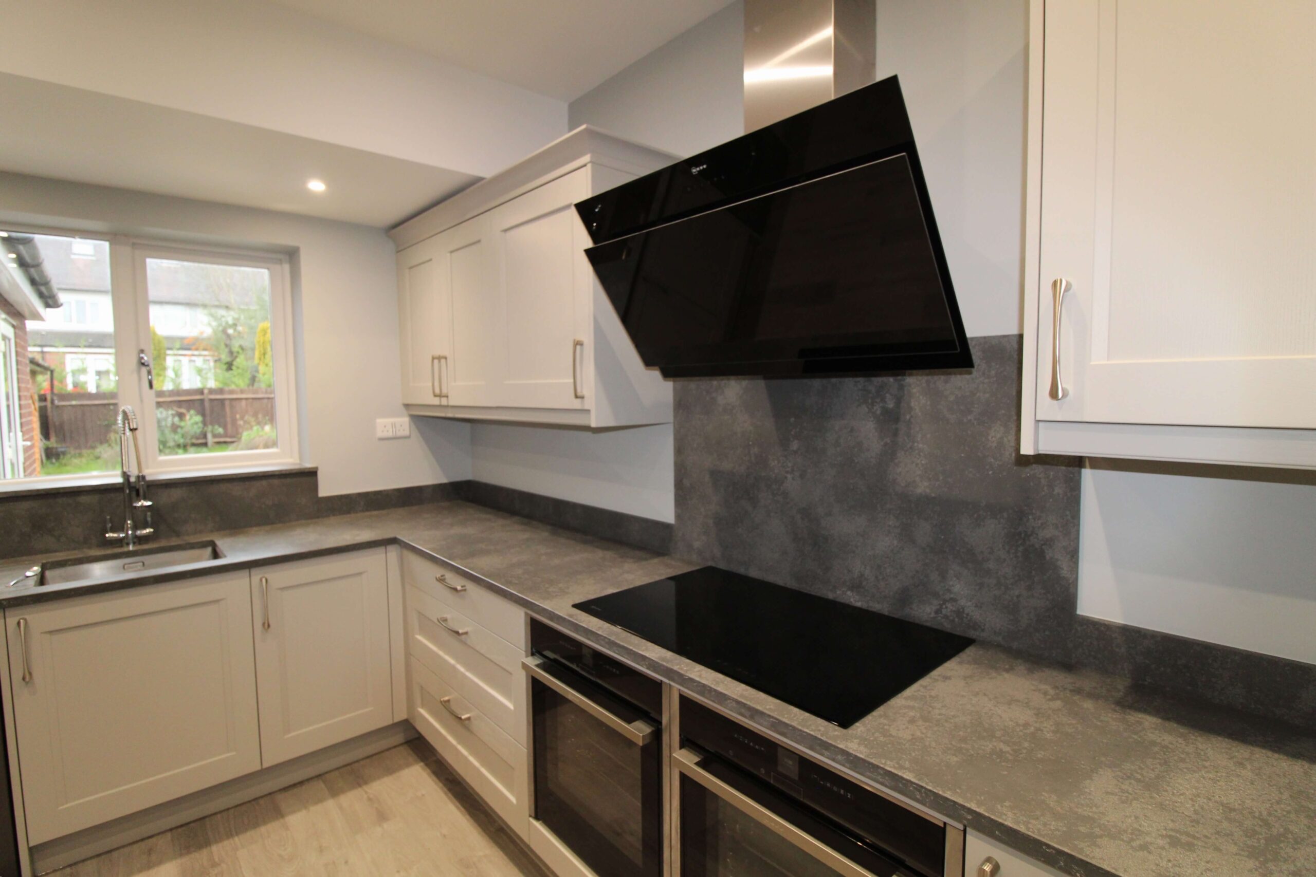 soft grey shaker kitchen with dark concrete worktop and neff oven, induction hob and extractor